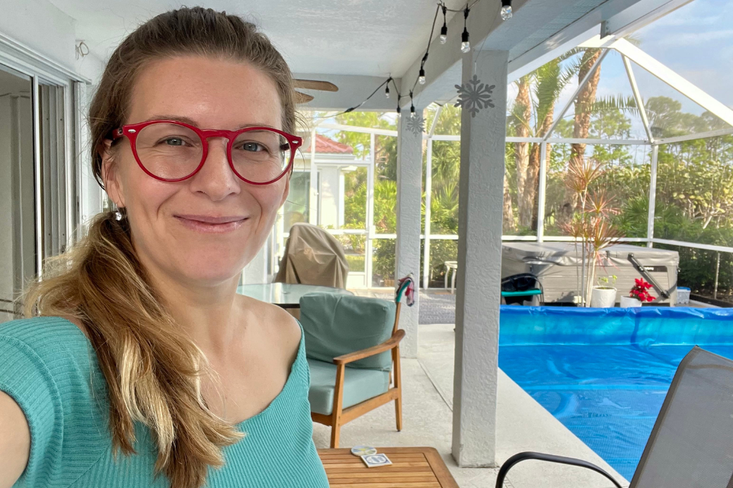 Woman with red glasses taking selfie by covered swimming pool. HomeExchange influencer.